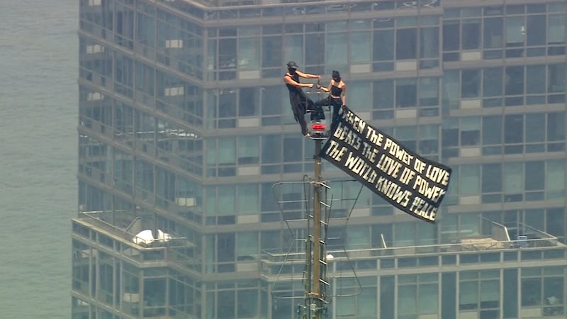 Aerial footage from WABC shows two people holding onto the building’s spire and raising a...